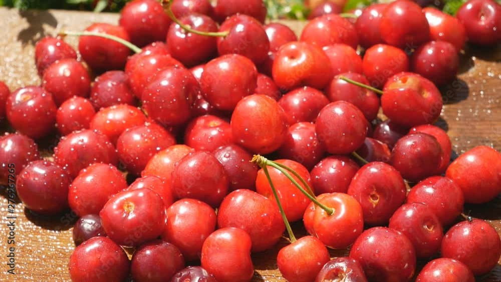 Red ripe sweet cherry closeup with water drops on a brown wooden background on the grass Red ripe sweet cherry closeup with water drops on a brown wooden background on the grass
