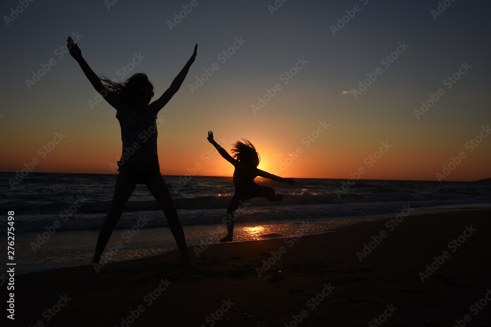 Silhouette of mother and son playing on the beach at the sunset.  Concept of family life and joy, summer vacations