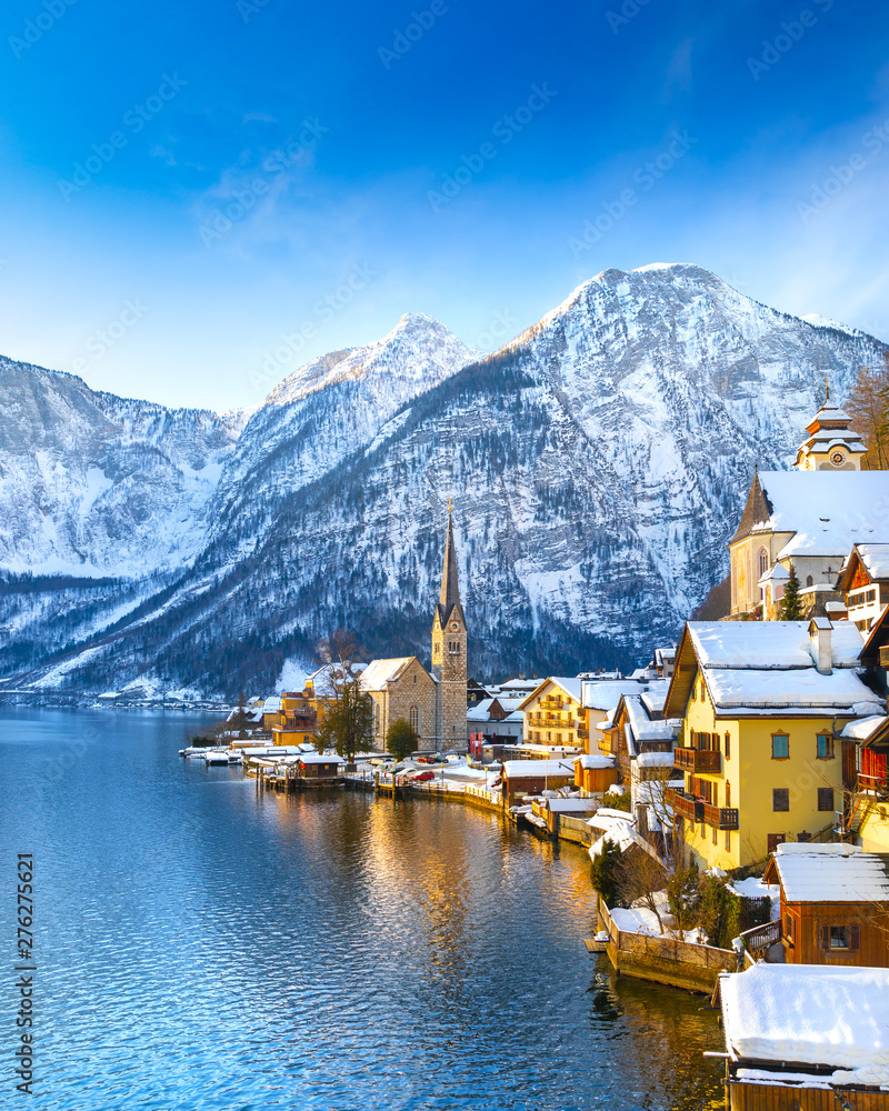 Classic postcard view of famous Hallstatt lakeside town in the Alps with traditional passenger ship on a beautiful cold sunny day with blue sky and clouds in winter, Austria