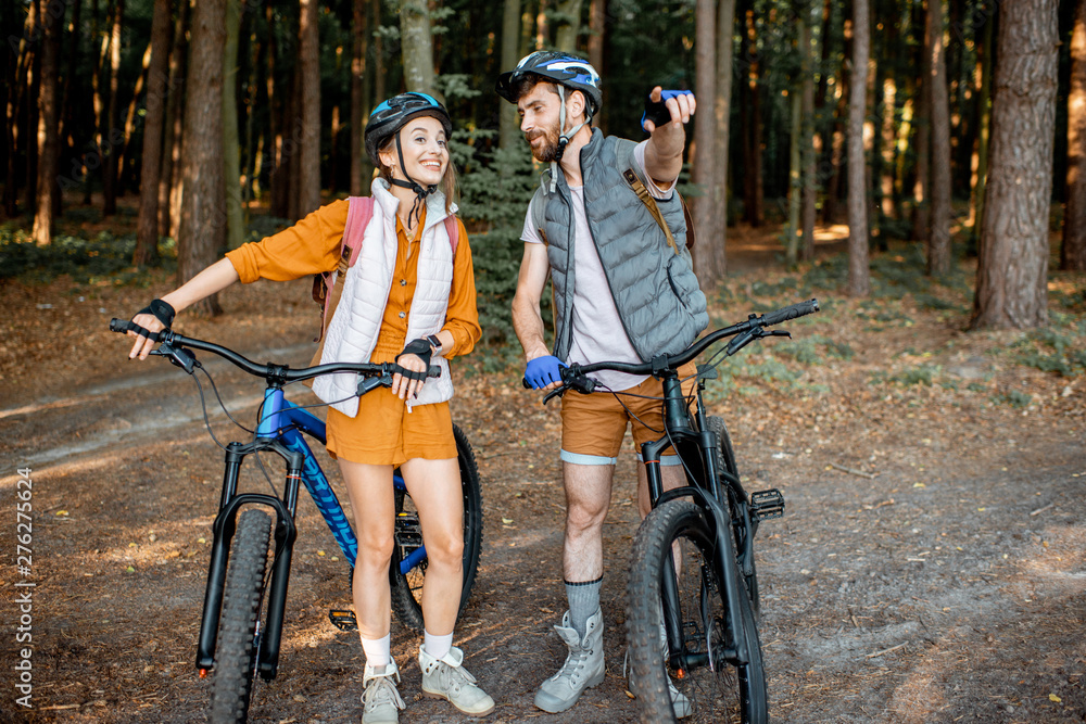 Obraz premium Young couple dressed casually standing together with mountain bicycles, traveling in the forest during the summer vacations