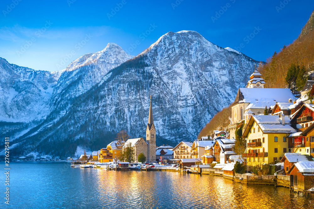 Classic postcard view of famous Hallstatt lakeside town in the Alps with traditional passenger ship on a beautiful cold sunny day with blue sky and clouds in winter, Austria