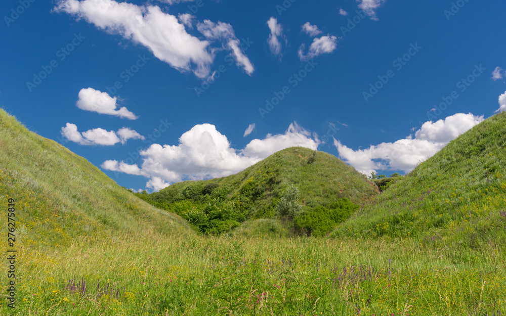 Blue skies, white clouds and hills overgrown with wild grasses in rural Ukrainian area
