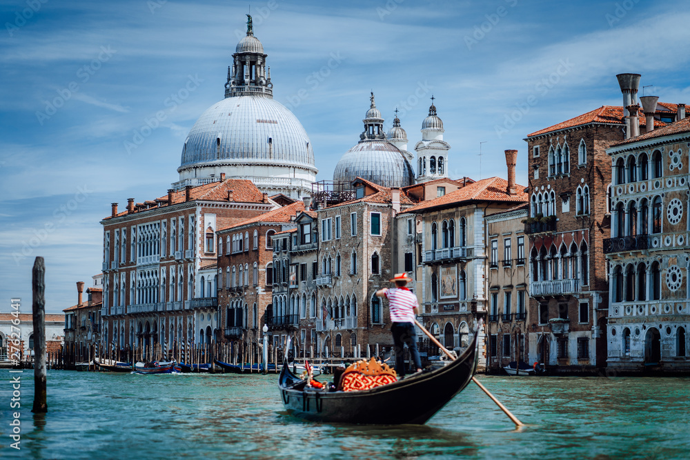 Traditional Gondola and gondolier on Canal Grande with Basilica di Santa Maria della Salute in the background in Venice, Italy. Summer vacation city trip