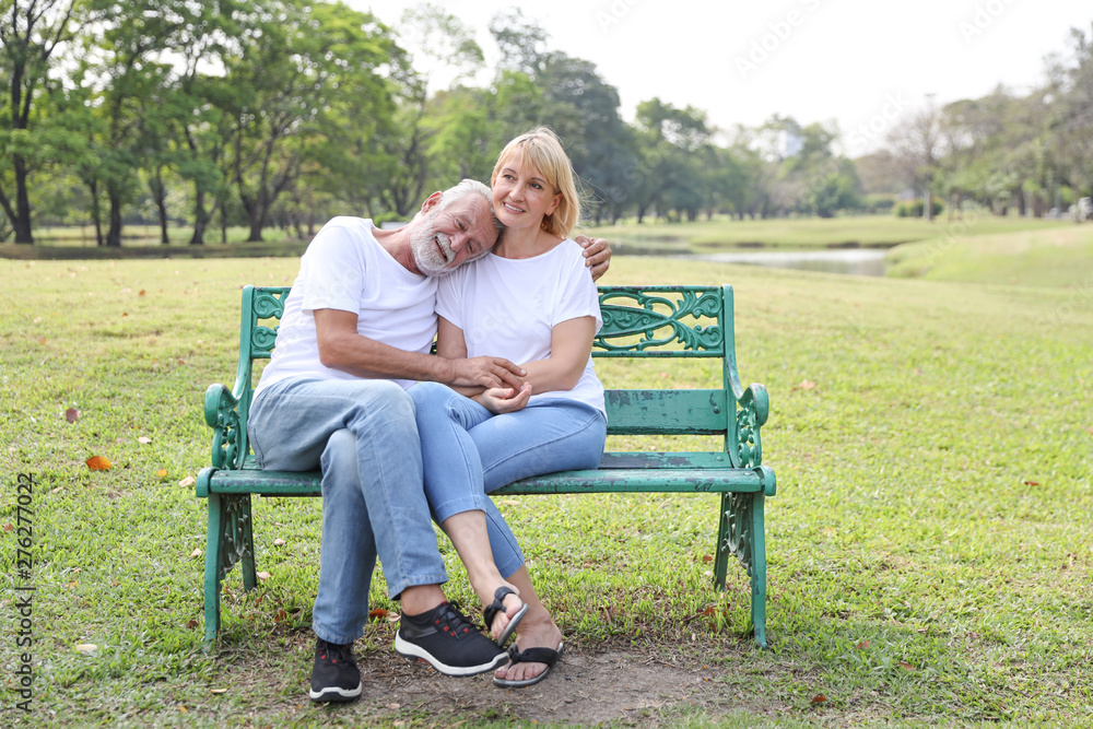 elderly couple with white shirt and blue jean sitting and embracing in park during summer time on wedding anniversary day