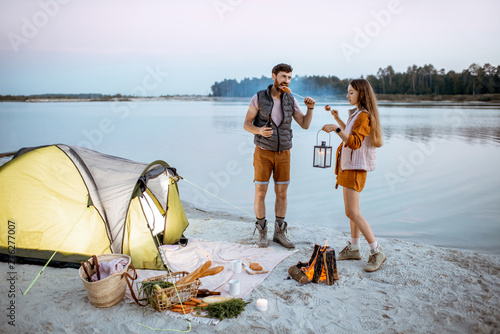 Young couple having fun at the campsite on the beach, standing near the fireplace during the evening