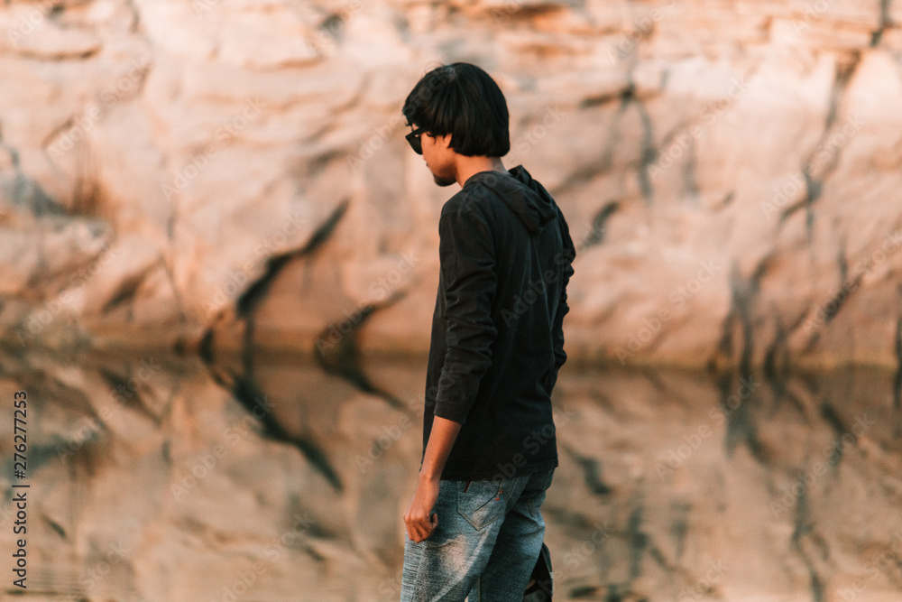 Indian model wearing sunglasses posing in front of the cliff besides lake Indian model wearing sunglasses posing in front of the cliff besides lake