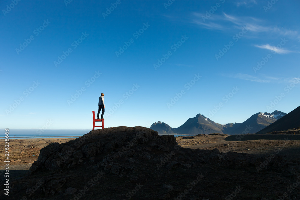 Girl on a red wooden chair on a empty stony landscape in Iceland