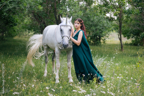 An elf with a unicorn. Beautiful girl in a green dress in nature with a white horse. Model in a medieval dress photo