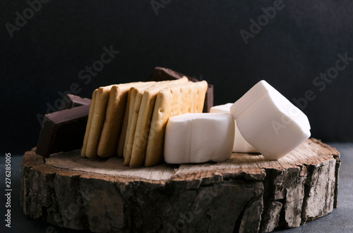 Closeup of ingredients for tasty s`mores with chocolate nad marshmallows on the wooden tray, rustic mood photo