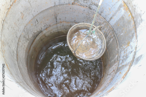 pulling out bucket full of drink water from the well, view of the water well, scooping water with buckets from water well