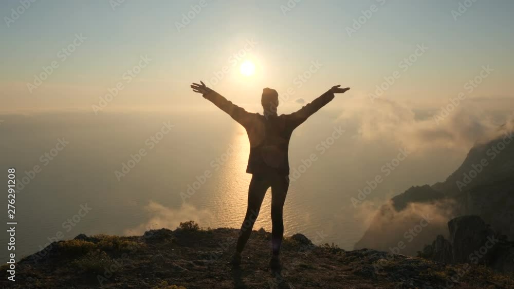 Silhuette Young Woman arms outstretched observing a beautiful dramatic sunset above a sea from a high mountain in Crimea. Silhuette Young Woman arms outstretched observing a beautiful dramatic sunset above a sea from a high mountain in Crimea.