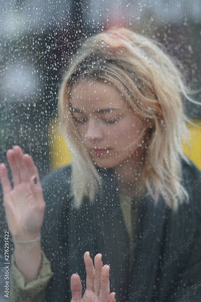 Woman looks through wet glass on a rainy day
