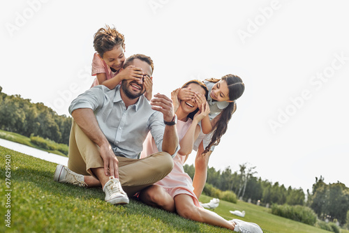 Guess who Happy young family of four smilin and having fun while sitting on grass in park