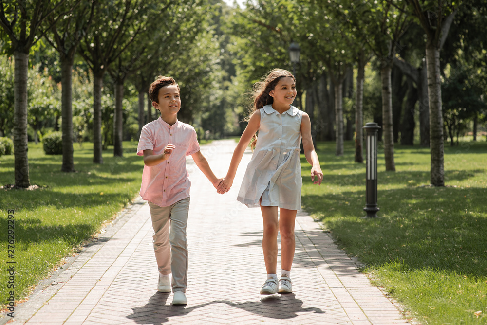 First love. Little boy and girl holding hands and smiling while walking outdoors in park First love. Little boy and girl holding hands and smiling while walking outdoors in park