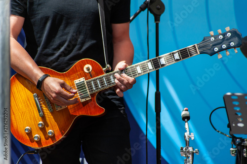 Young man in black neutral t-short plays yellow electric guitar on the outdoor stage, a day light