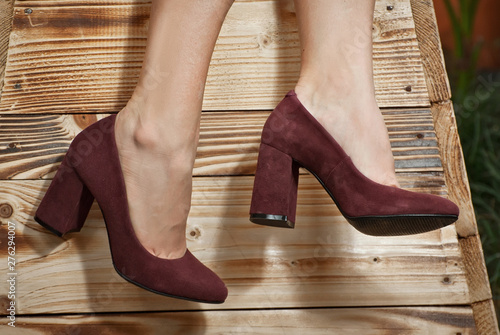 Red, burgundy suede shoes for women's leg. The girl walks in shoes. Classic shoes on the background of tropical plant arranger.