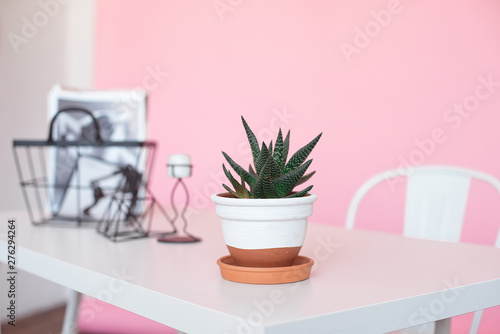 White table desk with copy space, supplies and a coffee mug pot with a flower on a pink background. Front view and copy space
