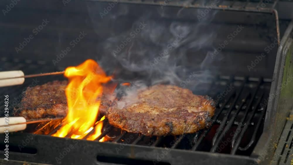 Two raw rib-eye steaks cooking on a grill. Two raw rib-eye steaks cooking on a grill.