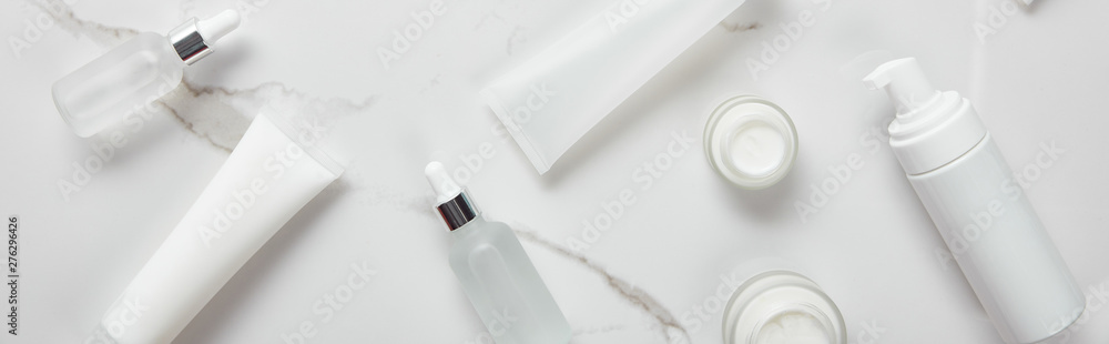 panoramic shot of cosmetic glass bottles, jars with cream, moisturizer tubes and dispenser on white surface panoramic shot of cosmetic glass bottles, jars with cream, moisturizer tubes and dispenser on white surface