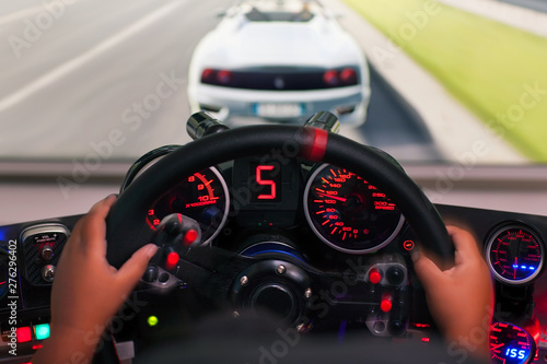 Hands of a kid on a steering wheel, while he plays a racing game in a realistic looking racing seat with gauges.