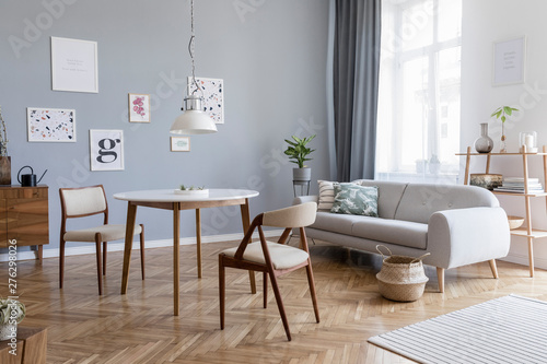 Design scandinavian home interior of open space with stylish chairs  family table wooden commode  gray sofa  accessories and mock up posters gallery wall. Gray background walls. Retro cozy home decor.