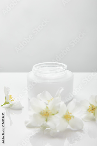 jasmine flowers on white surface near jar with cream