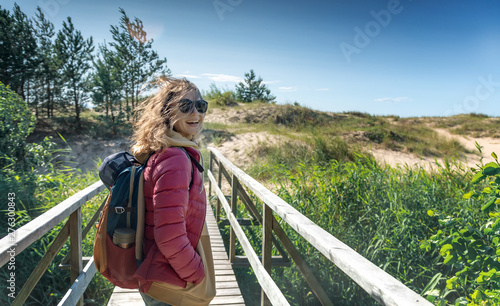 Young happy beautiful girl walks along the cold shore of the Baltic Sea in windy sunny weather, traveling to the Scandinavian countries