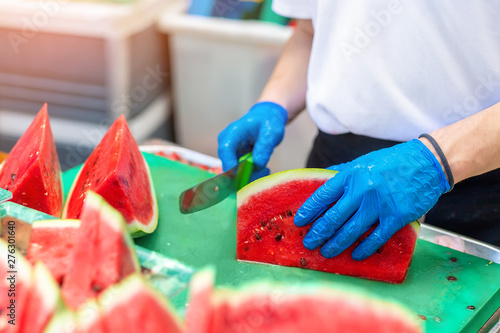 Cook in rubber gloves peeling and slicing gresh tasty juicy sliced watermelon for hotel guests at tropical resort outdoors photo