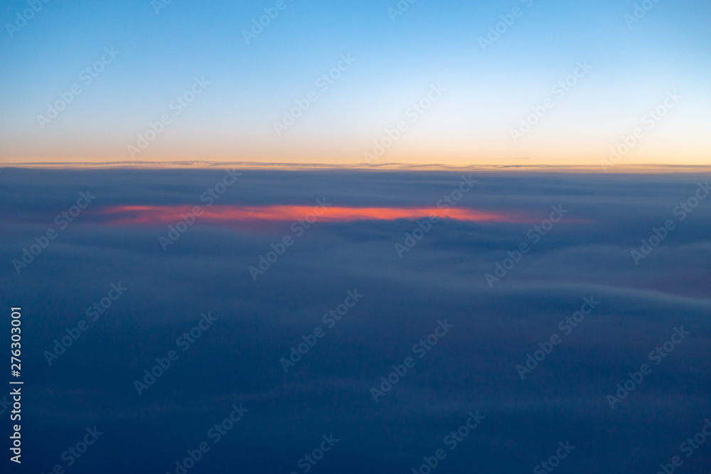 Cloudscape from above. View through a window of a modern jet airliner during sunset hours. Cloudscape from above. View through a window of a modern jet airliner during sunset hours.