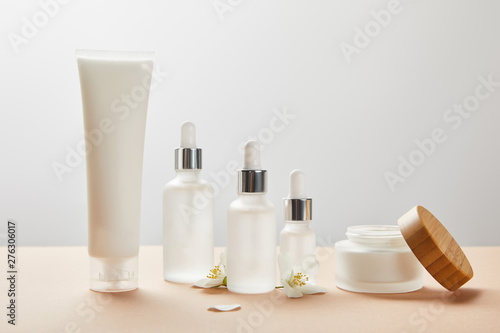 cream tube, cosmetic glass bottles, open jar with cream and few jasmine flowers on beige photo
