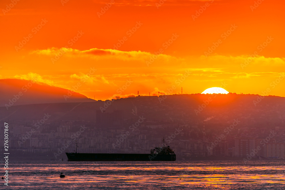 Beautiful sunset amongst the clouds. The sun rays are simply beautiful. City, mountains and ships in sea