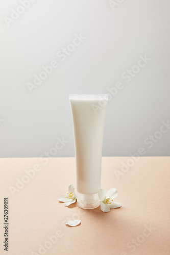 cream tube with hand cream and few jasmine flowers on beige