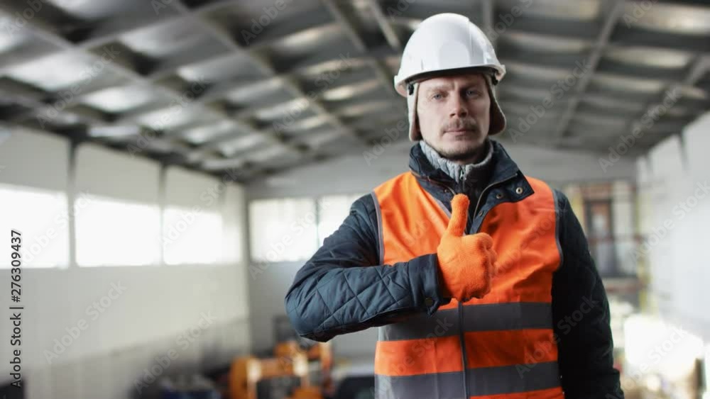 man beard and mustache in a hard hat and overalls is standing in the middle of the hangar and showing thumbs up at the camera man beard and mustache in a hard hat and overalls is standing in the middle of the hangar and showing thumbs up at the camera