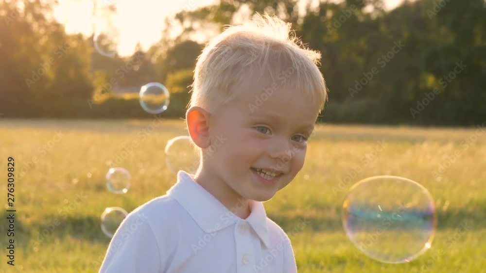 Cute little boy in white polo-shirt playing outdoors, blowing soap bubbles, having fun in a park. Summer, sunny Cute little boy in white polo-shirt playing outdoors, blowing soap bubbles, having fun in a park. Summer, sunny