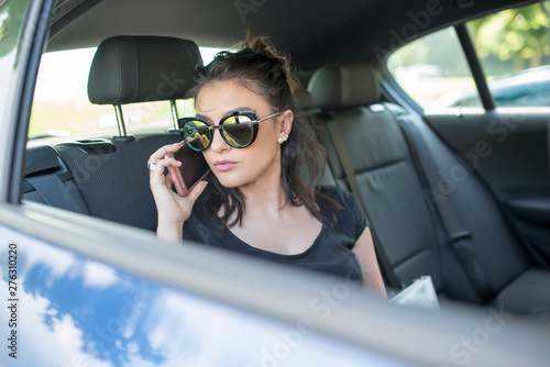 Close up portrait of happy young caucasian woman sitting in car talking on cellphone.
