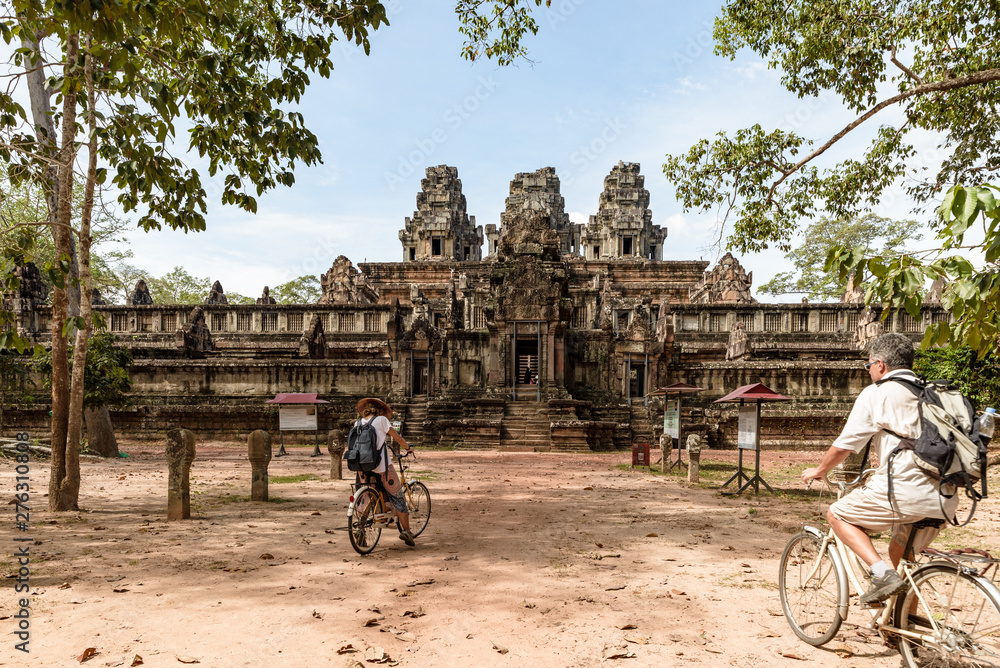 Obraz premium Tourist couple cycling around Angkor temple, Cambodia. Ta Keo building ruins in the jungle. Eco friendly tourism traveling, toned image.