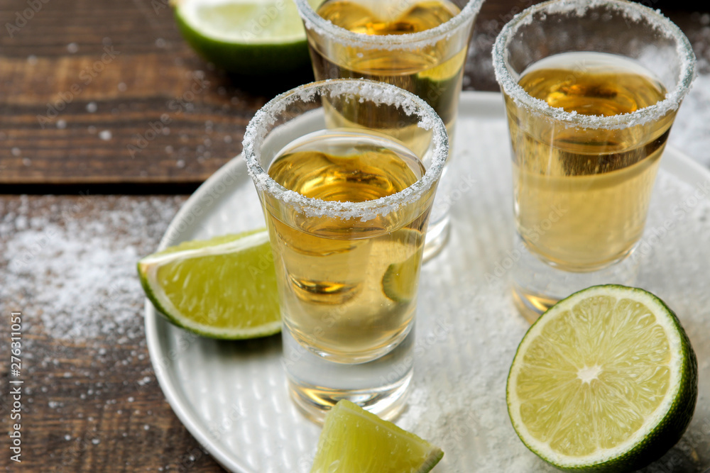 Gold tequila in a glass with salt and lime on a brown wooden table. alcoholic beverages. Gold tequila in a glass with salt and lime on a brown wooden table. alcoholic beverages.