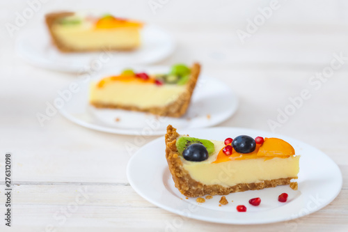 A few slices of cheesecake with fruit on white plates.