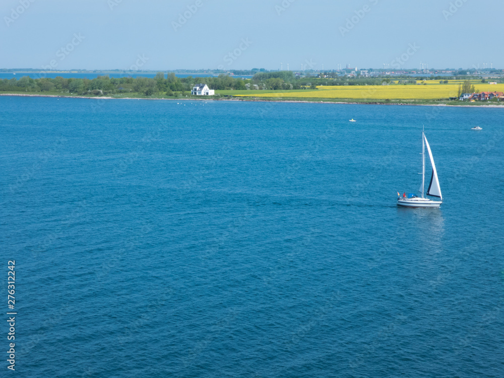 Fototapeta premium ein einsames Segelboot fährt durch den Fehmarn Sund; im Hintergrund die Insel Fehmarn