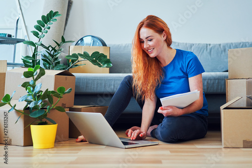 Foto Happy young woman paying bills with laptop while sitting on floor in new apartme