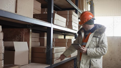 responsible worker in a helmet and overalls stands next to the racks and takes inventory with the ipad
