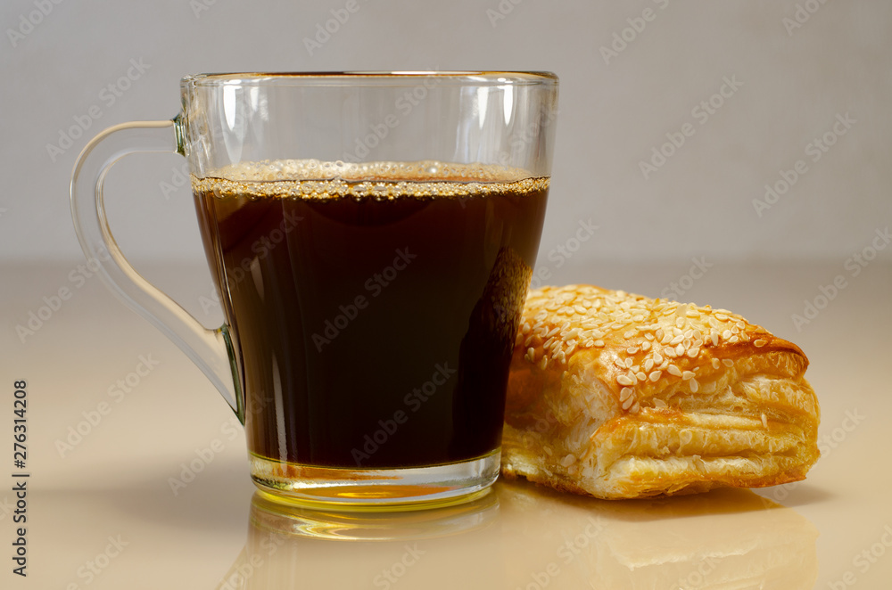 Coffee in a transparent cup. Puff bun with sesame on a glass surface. Bubbles in coffee Coffee in a transparent cup. Puff bun with sesame on a glass surface. Bubbles in coffee