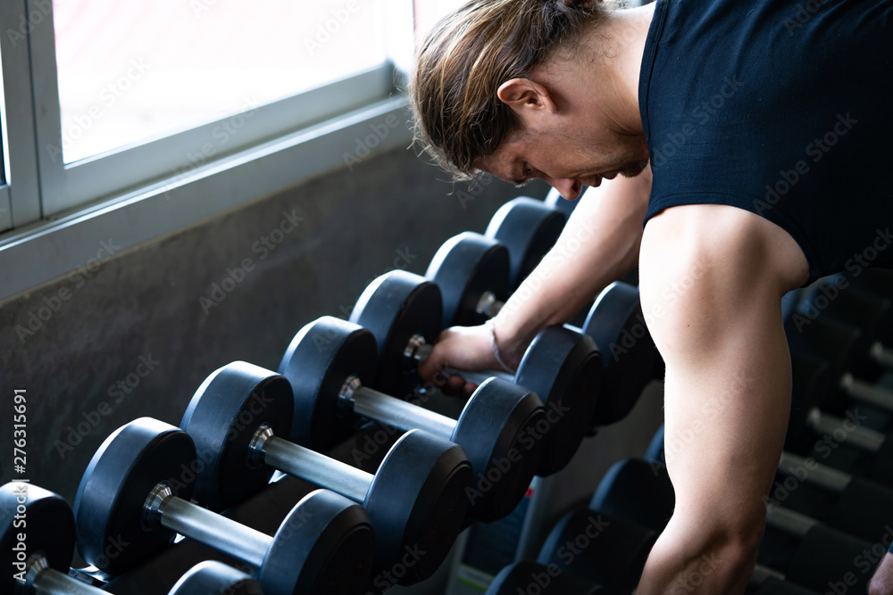 Selective focus of bodybuilder man in black sportswear holding and taking  heavy weight dumbbell out off dumbbell rack for weight training exercise in  fitness gym. Strong and healthy lifestyle concept. Stock Photo
