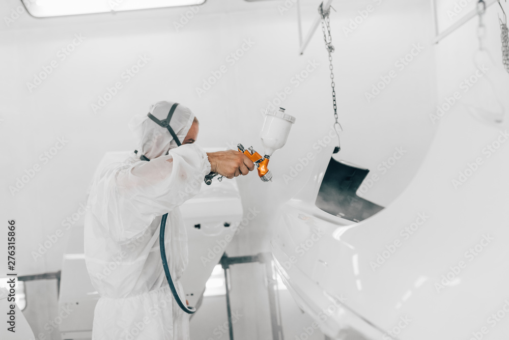 Worker in protective uniform painting car parts with white base paint. - obrazy, fototapety, plakaty 