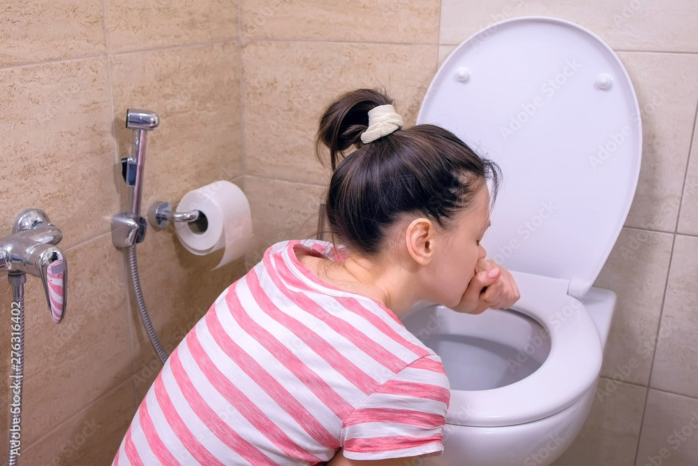 Pregnant young tired woman is vomiting in toilet sitting on the floor at home in morning, back
