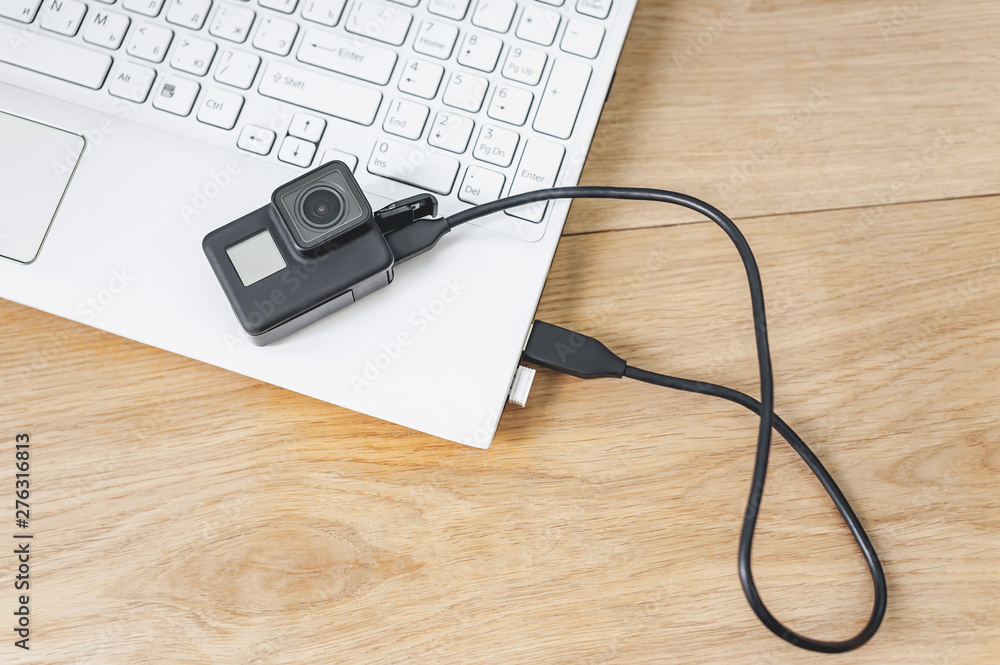Action camera connected to a white laptop, against the background of a wooden table. Action camera connected to a white laptop, against the background of a wooden table.