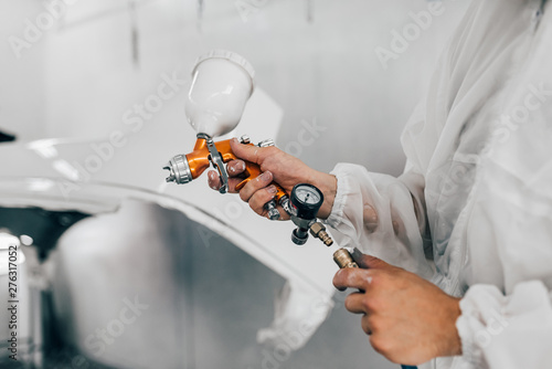 Close-up image of man holding spray gun and painting a car. photo