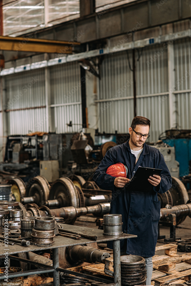 Fototapeta premium Manual worker looking at clipboard at metal manufacturing plant. Production of steel train wheels.