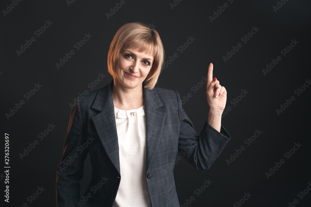 Woman in a jacket pointing something on the dark grey background Woman in a jacket pointing something on the dark grey background