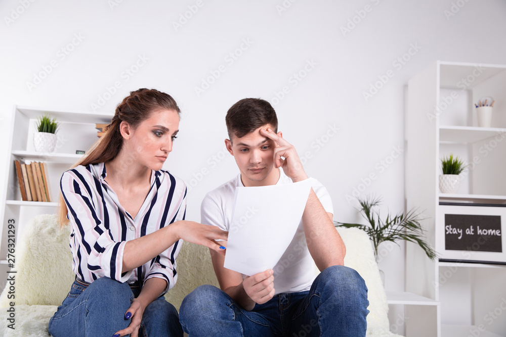 Happy couple reading mail and checking accountancy looking each other sitting on a couch at home Happy couple reading mail and checking accountancy looking each other sitting on a couch at home